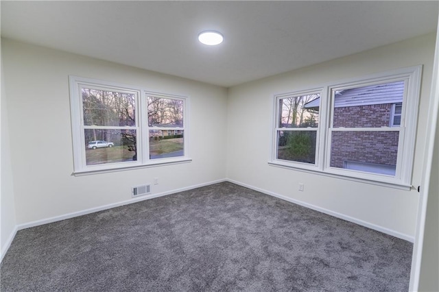 spare room featuring a wealth of natural light, baseboards, visible vents, and dark colored carpet