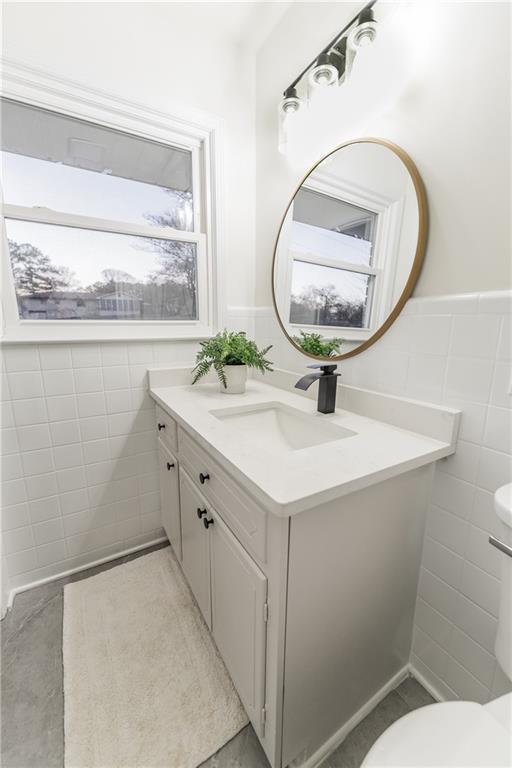 half bathroom with wainscoting, toilet, tile patterned floors, vanity, and tile walls