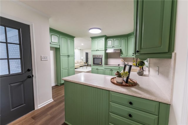 kitchen with oven, under cabinet range hood, dark wood-style flooring, baseboards, and light countertops