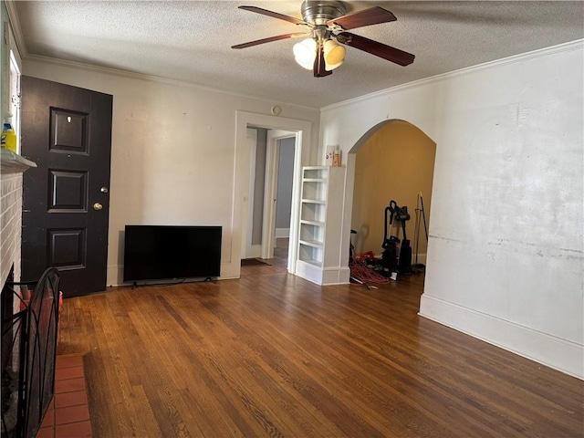 living area with a brick fireplace, crown molding, wood finished floors, arched walkways, and a textured ceiling