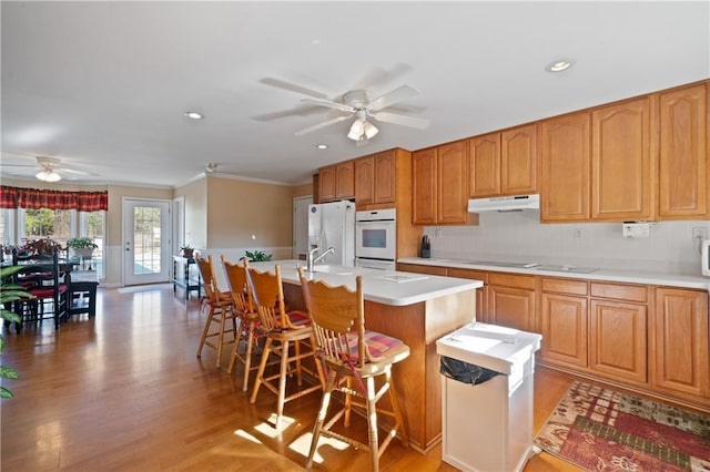 kitchen featuring a breakfast bar, white appliances, ornamental molding, an island with sink, and light hardwood / wood-style floors