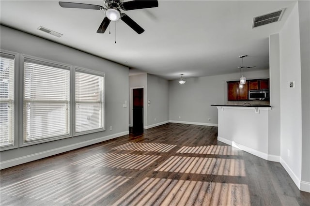 unfurnished living room with a ceiling fan, dark wood-style flooring, visible vents, and baseboards