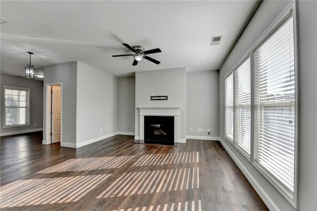 unfurnished living room with ceiling fan with notable chandelier, a fireplace with flush hearth, visible vents, baseboards, and dark wood-style floors