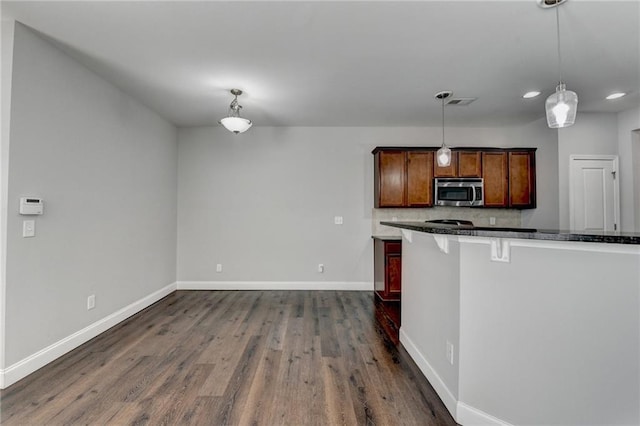 kitchen with dark wood-style flooring, baseboards, hanging light fixtures, stainless steel microwave, and dark countertops