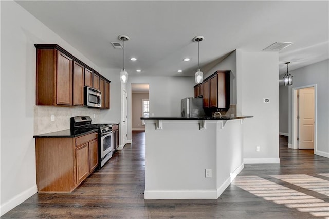 kitchen with visible vents, appliances with stainless steel finishes, a breakfast bar, dark wood-type flooring, and backsplash