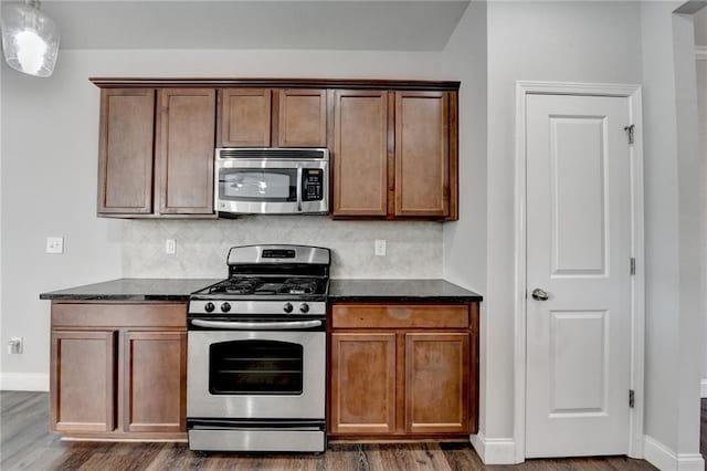 kitchen featuring tasteful backsplash, dark stone countertops, stainless steel appliances, and dark wood-type flooring