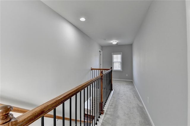 corridor featuring baseboards, an upstairs landing, and light colored carpet