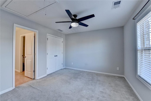 carpeted spare room with attic access, visible vents, ceiling fan, and baseboards