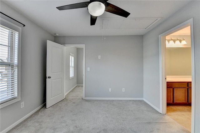 unfurnished bedroom featuring light colored carpet, a ceiling fan, baseboards, ensuite bath, and attic access