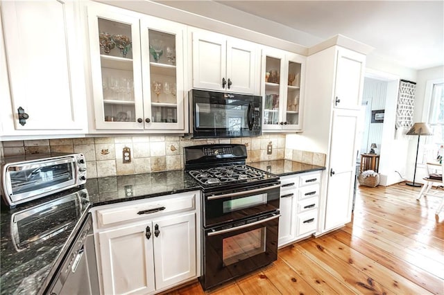 kitchen featuring white cabinetry, light wood-type flooring, dark stone counters, decorative backsplash, and black appliances