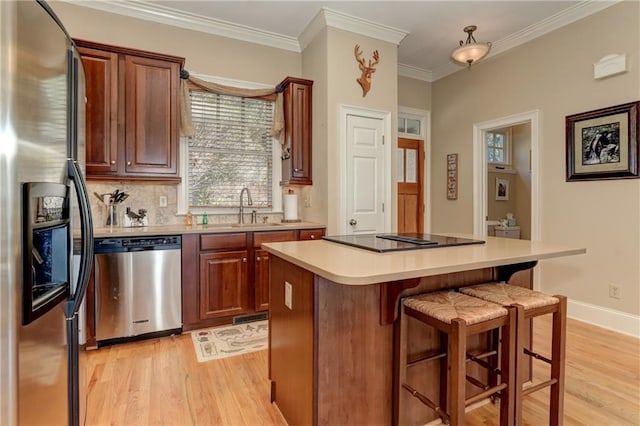 kitchen featuring a kitchen island, appliances with stainless steel finishes, light wood-type flooring, ornamental molding, and sink