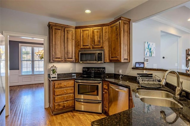 kitchen with light wood-style flooring, a wainscoted wall, stainless steel appliances, a sink, and brown cabinets