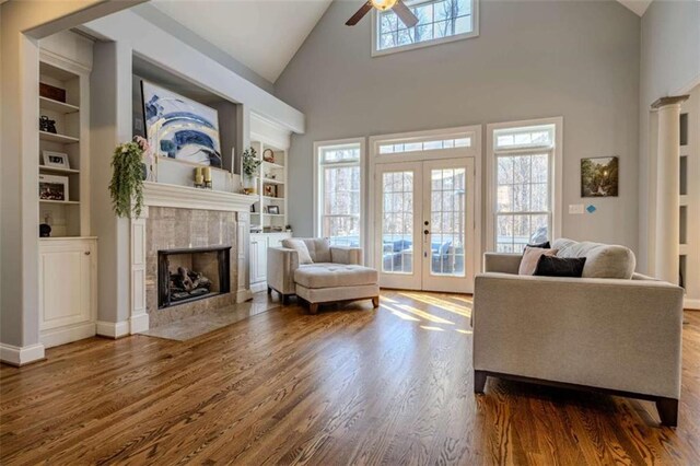 living area featuring built in shelves, a tile fireplace, wood finished floors, a ceiling fan, and french doors