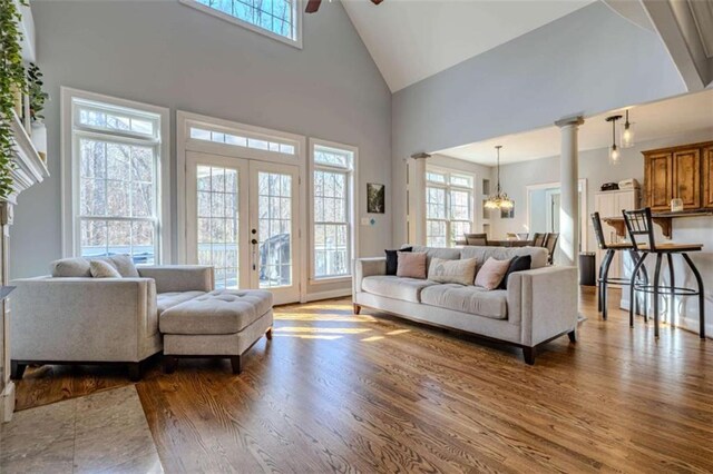 living room featuring wood finished floors, french doors, ornate columns, high vaulted ceiling, and ceiling fan with notable chandelier