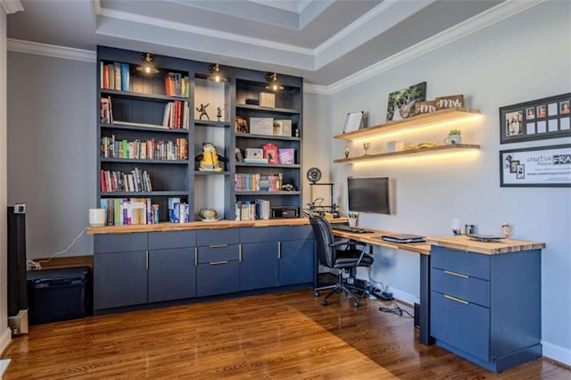 office space with baseboards, a raised ceiling, ornamental molding, dark wood-style flooring, and built in shelves