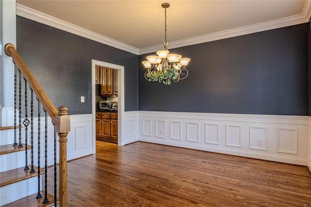 spare room with dark wood-style flooring, a wainscoted wall, crown molding, stairway, and an inviting chandelier