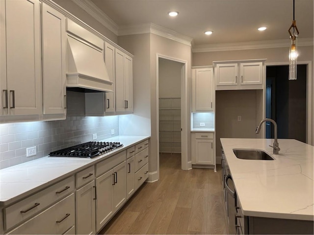 kitchen with a sink, premium range hood, ornamental molding, and light wood finished floors