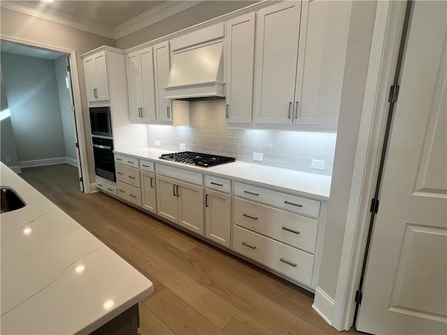kitchen with ornamental molding, wood finished floors, oven, premium range hood, and stainless steel gas stovetop