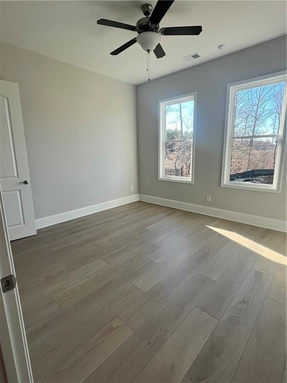 unfurnished room with ceiling fan, baseboards, visible vents, and wood finished floors