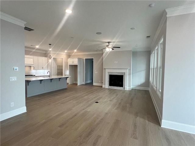 unfurnished living room featuring a sink, baseboards, ceiling fan, and ornamental molding
