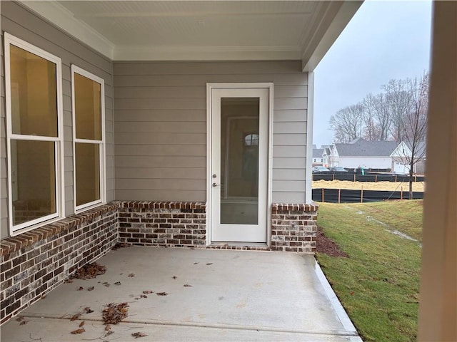 view of exterior entry featuring brick siding and a patio area