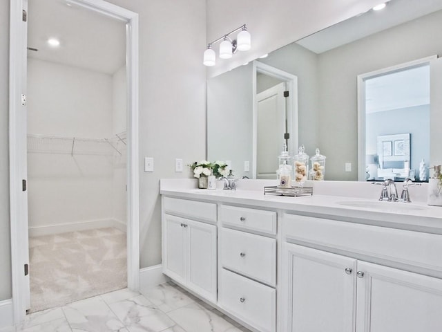 ensuite bathroom with double vanity, a walk in closet, a sink, and marble finish floor