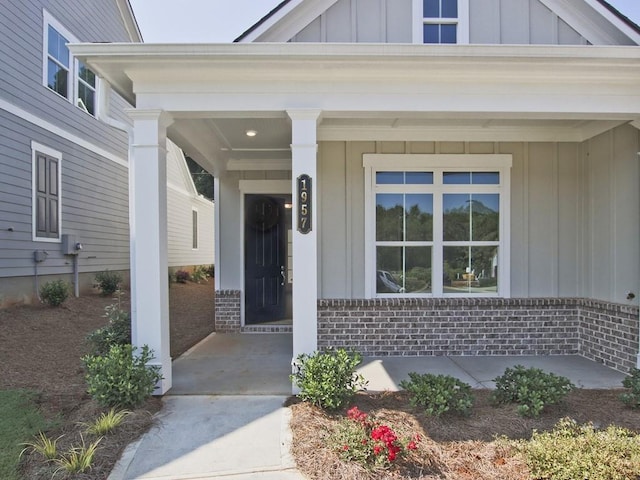 view of exterior entry with board and batten siding, brick siding, and covered porch