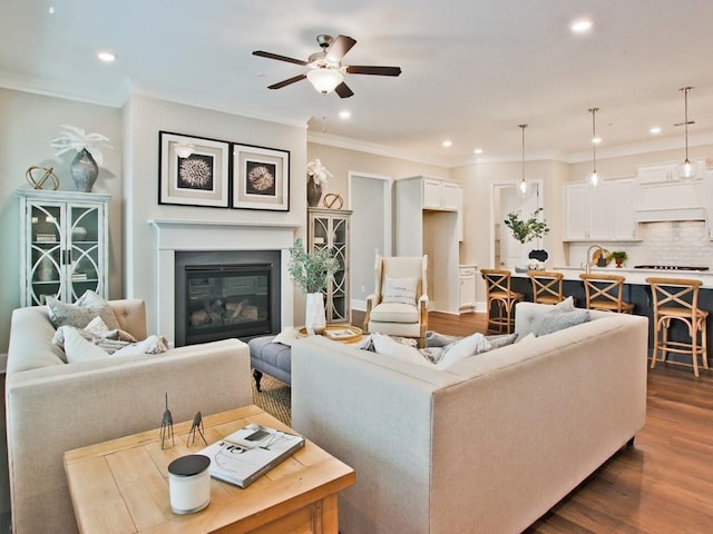 living area featuring crown molding, dark wood-style flooring, ceiling fan, a glass covered fireplace, and recessed lighting