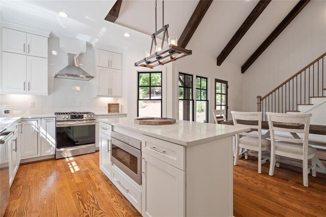 kitchen with white cabinetry, beamed ceiling, wall chimney range hood, and appliances with stainless steel finishes