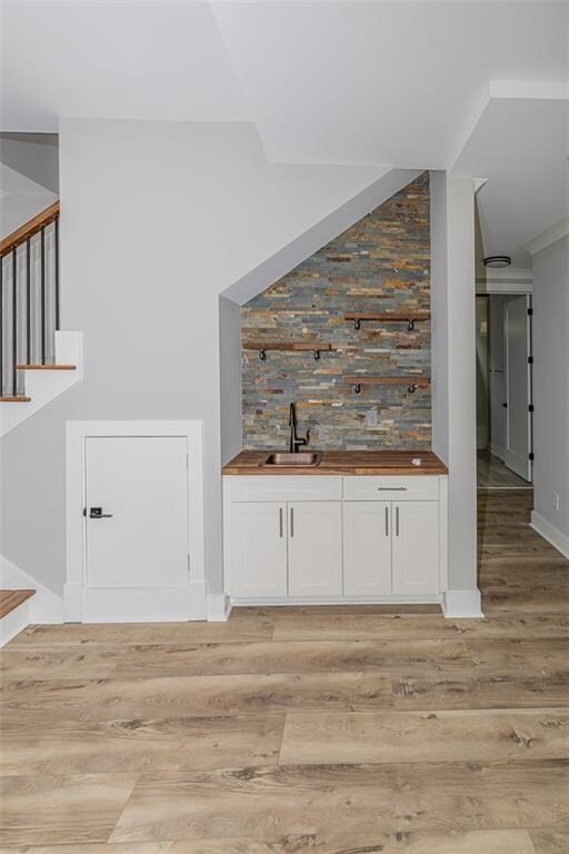 bar with butcher block countertops, white cabinetry, light hardwood / wood-style floors, and sink