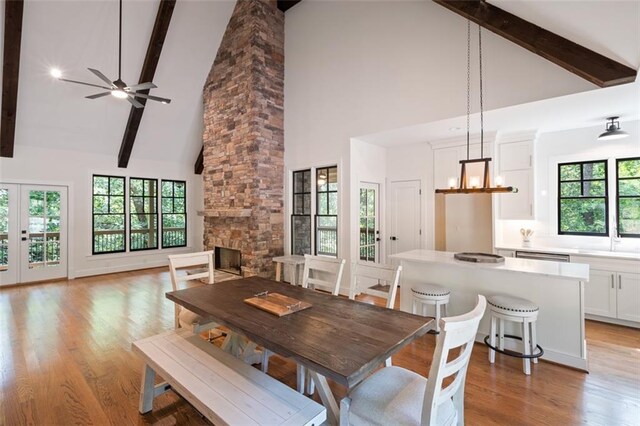 dining space with a stone fireplace, beamed ceiling, high vaulted ceiling, light hardwood / wood-style floors, and ceiling fan with notable chandelier