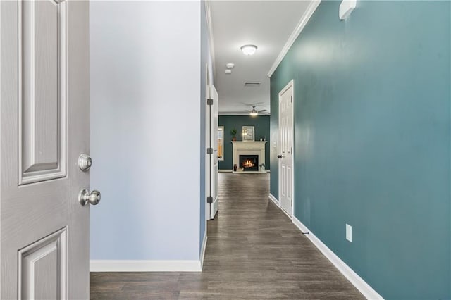 hallway with dark wood-type flooring, baseboards, ornamental molding, and visible vents