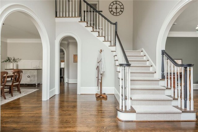 foyer featuring stairs, a high ceiling, wood finished floors, and arched walkways