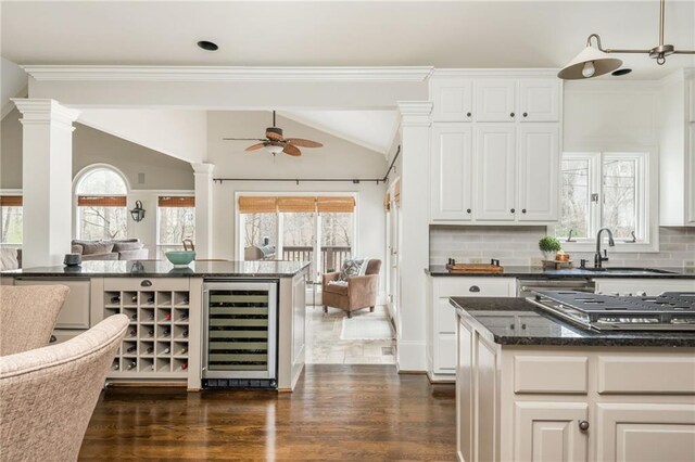 dining room featuring wine cooler, a ceiling fan, a warm lit fireplace, ornate columns, and dark wood-style flooring