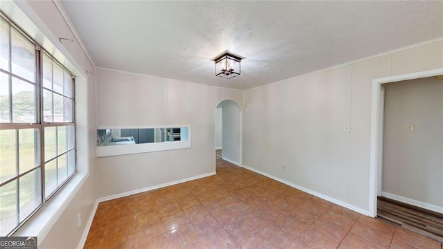 empty room featuring arched walkways, a textured ceiling, baseboards, and crown molding