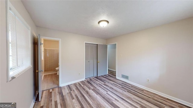 unfurnished bedroom featuring baseboards, visible vents, ensuite bathroom, light wood-style floors, and a closet