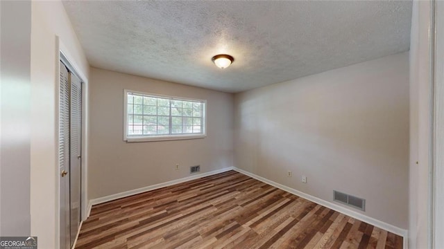 unfurnished bedroom with a textured ceiling, a closet, wood finished floors, and visible vents