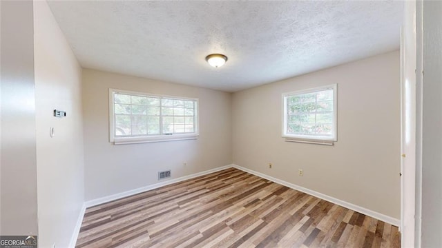 empty room with baseboards, light wood-style flooring, visible vents, and a textured ceiling