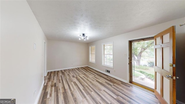 empty room featuring visible vents, baseboards, light wood-style flooring, and a textured ceiling