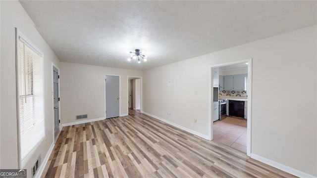 spare room with a textured ceiling, light wood finished floors, visible vents, and baseboards