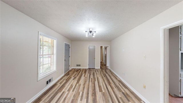 interior space featuring light wood-style floors, baseboards, visible vents, and a textured ceiling