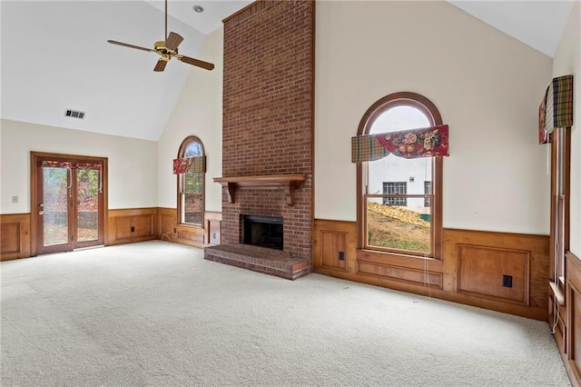 unfurnished living room with visible vents, wainscoting, a brick fireplace, and carpet floors