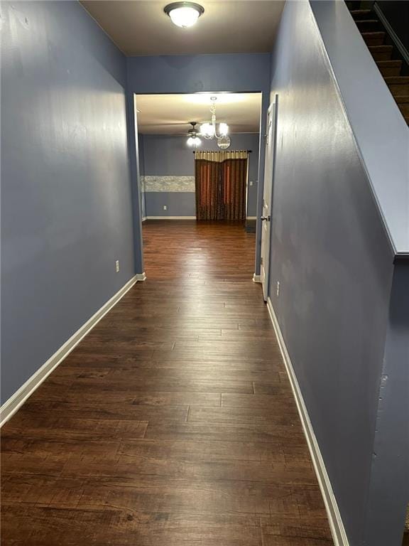 corridor with dark wood-type flooring and an inviting chandelier