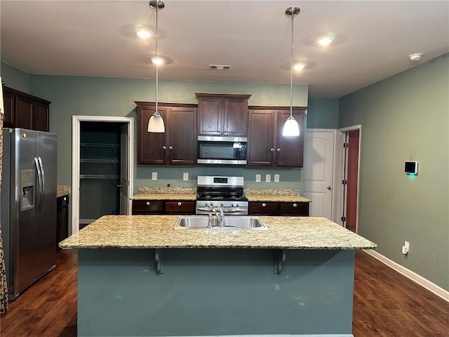 kitchen with pendant lighting, a kitchen island with sink, stainless steel appliances, and dark hardwood / wood-style floors