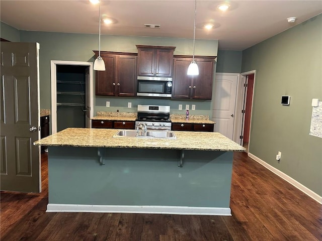 kitchen with stainless steel appliances, decorative light fixtures, a kitchen bar, and an island with sink