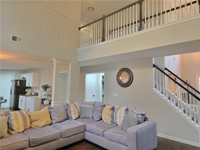 living room featuring visible vents, baseboards, stairs, dark wood-style floors, and decorative columns