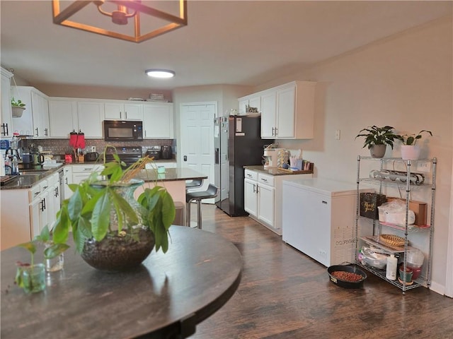 kitchen featuring tasteful backsplash, black microwave, white cabinetry, and fridge