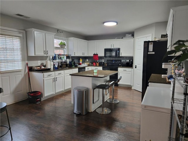 kitchen with visible vents, dark countertops, a center island, black appliances, and white cabinetry