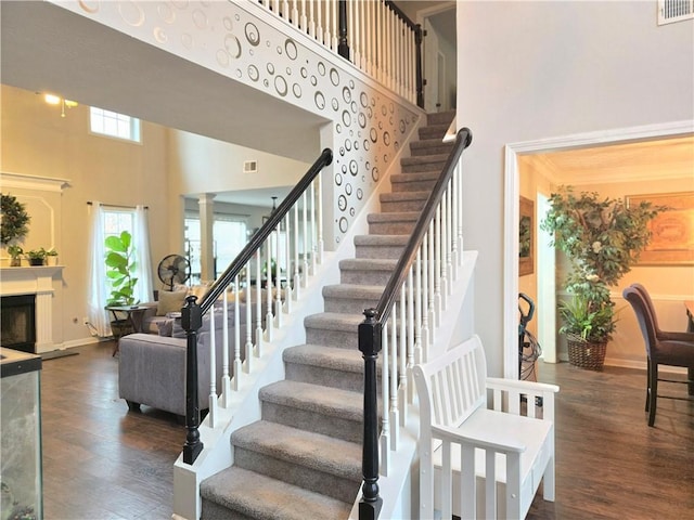 stairs featuring visible vents, a fireplace with raised hearth, a towering ceiling, and wood finished floors