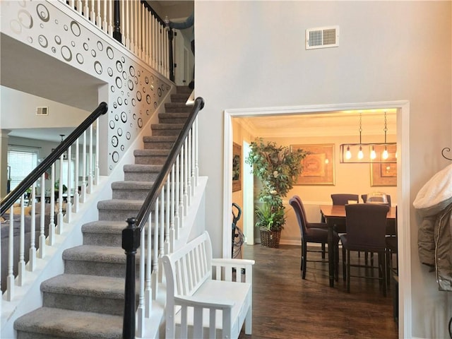 staircase featuring wood finished floors, a towering ceiling, visible vents, and baseboards